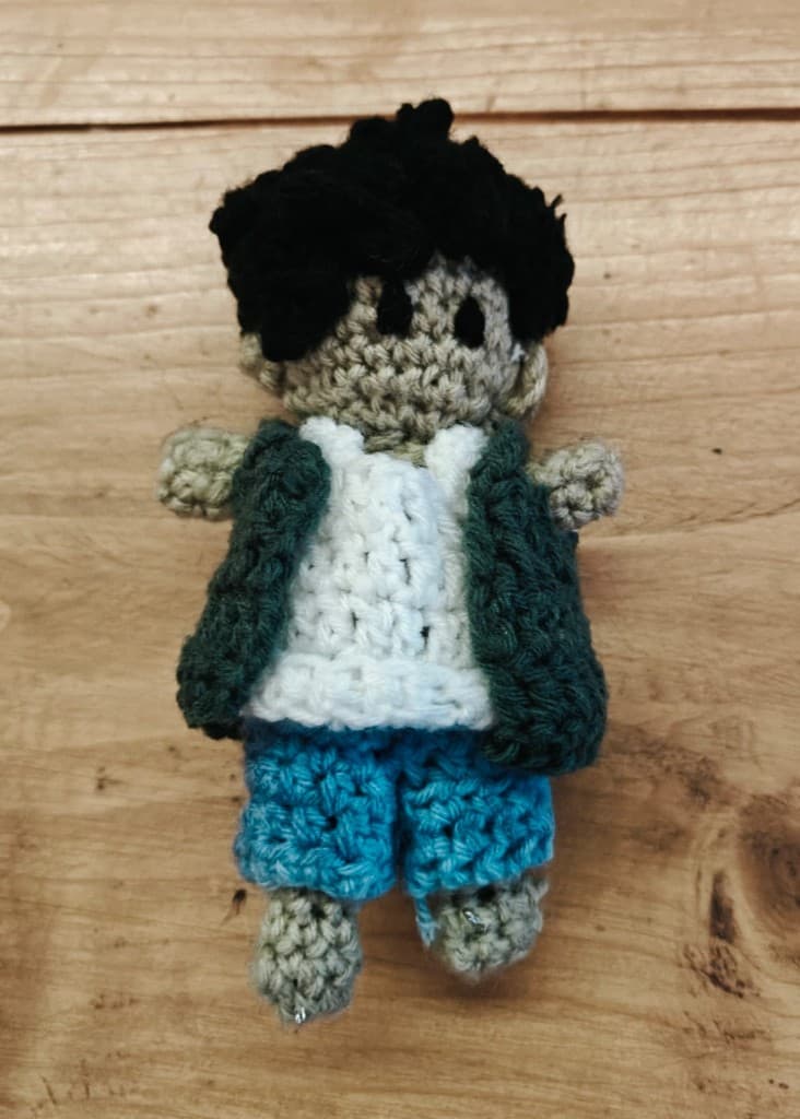 Handmade crochet doll wearing a white vest, green cardigan, and blue shorts