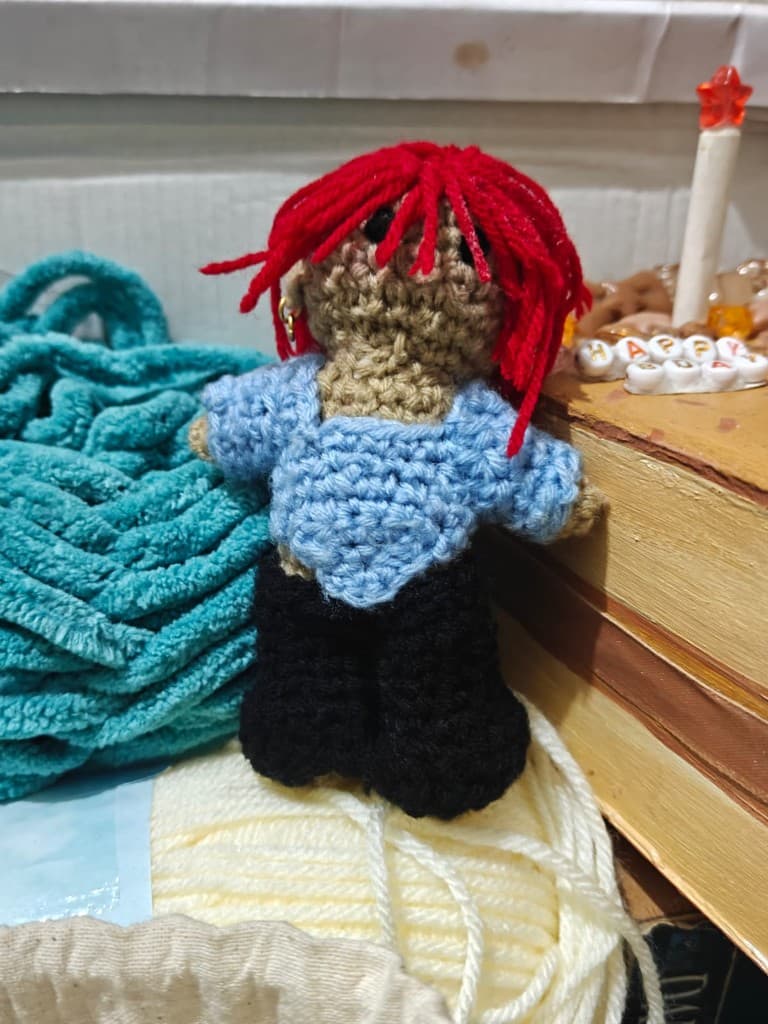 Handmade crochet doll with shaggy red hair, a gold hoop earring, a light blue top, and black legs